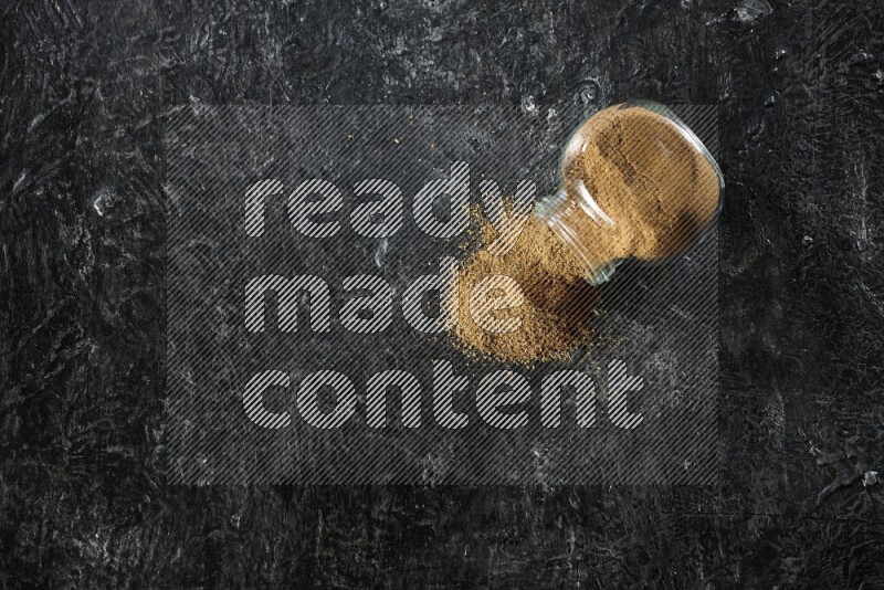 وعاء زجاجي مقلوب ممتلئ ببودرة الكمون والبودرة تناثرت منه على خلفية سوداء