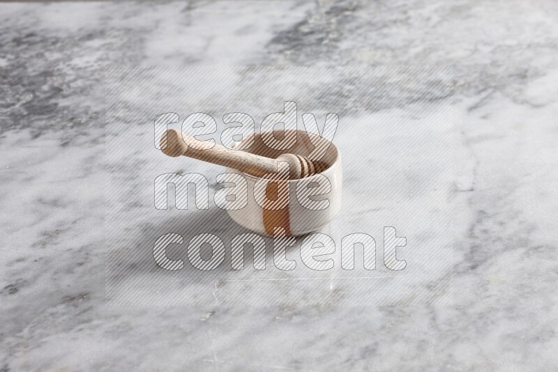 Multicolored pottery bowl with wooden honey dipper in it on grey marble background