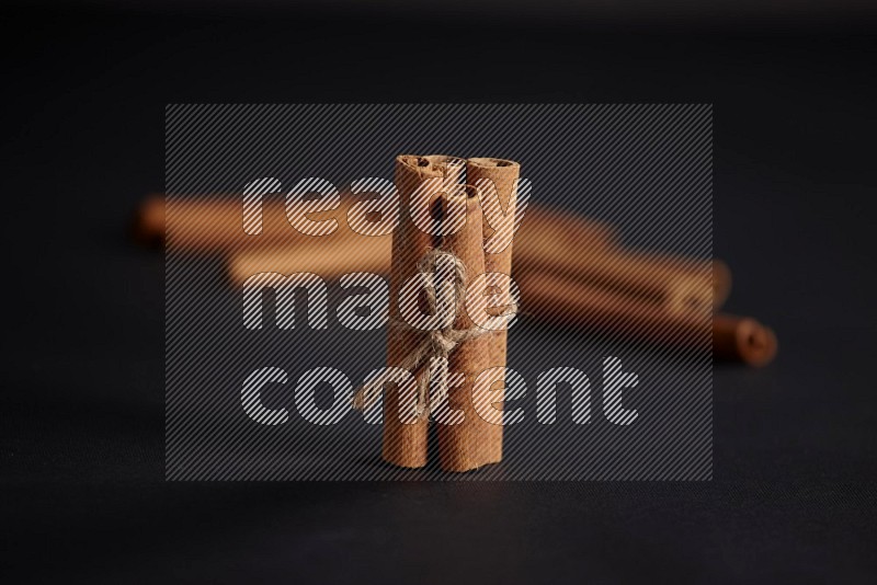 4 Cinnamon sticks stacked and bounded with more sticks in the background on black flooring