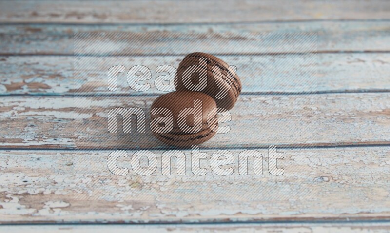 45º Shot of two Brown Dark Chocolate macarons on light blue wooden background