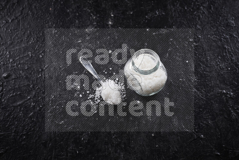 A glass jar full of coarse sea salt crystals on black background