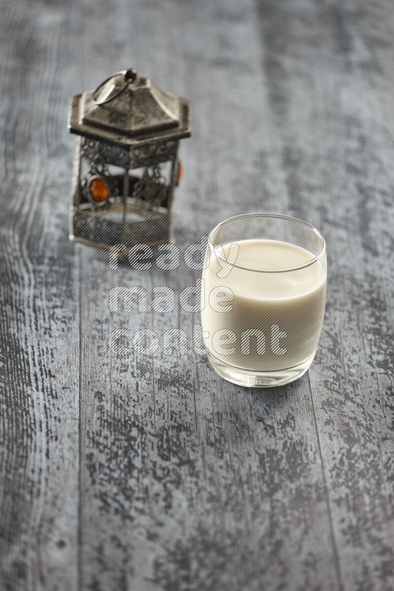 A silver lantern with different drinks, dates, nuts, prayer beads and quran on grey wooden background