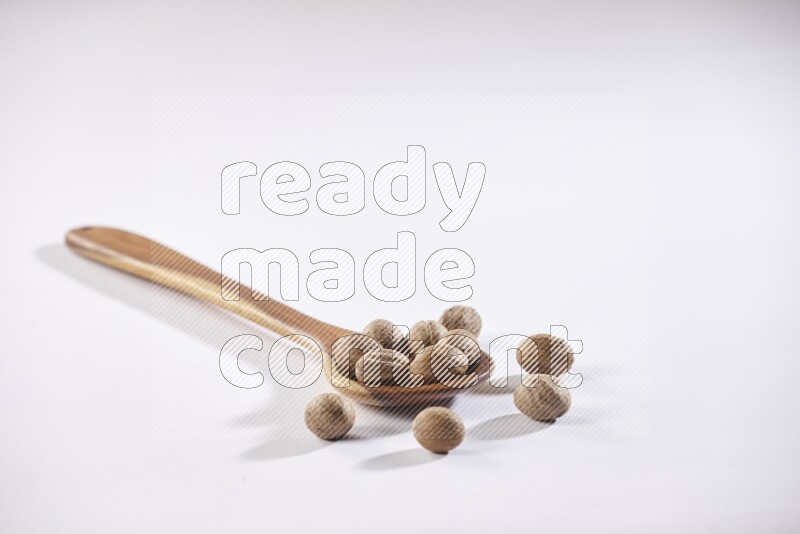 A wooden ladle full of whole nutmeg seeds on a white flooring
