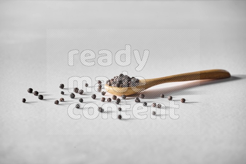 A wooden spoon full of black pepper on white flooring