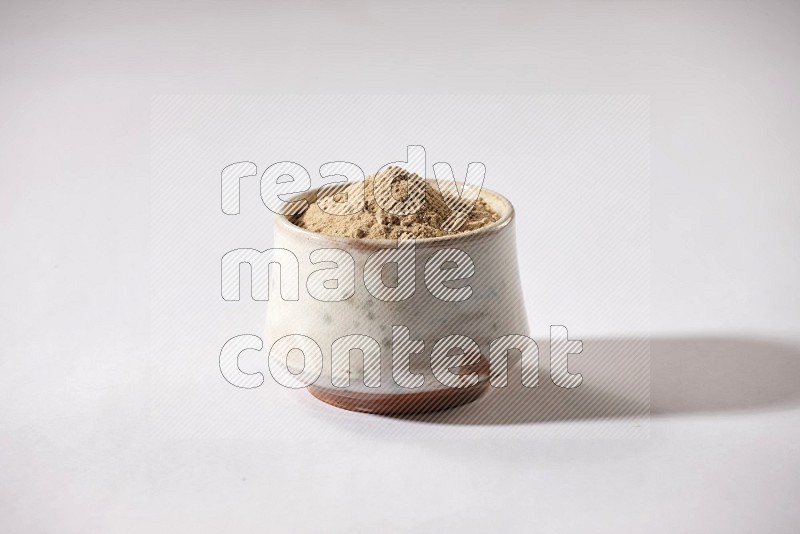 A beige pottery bowl full of garlic powder on a white flooring