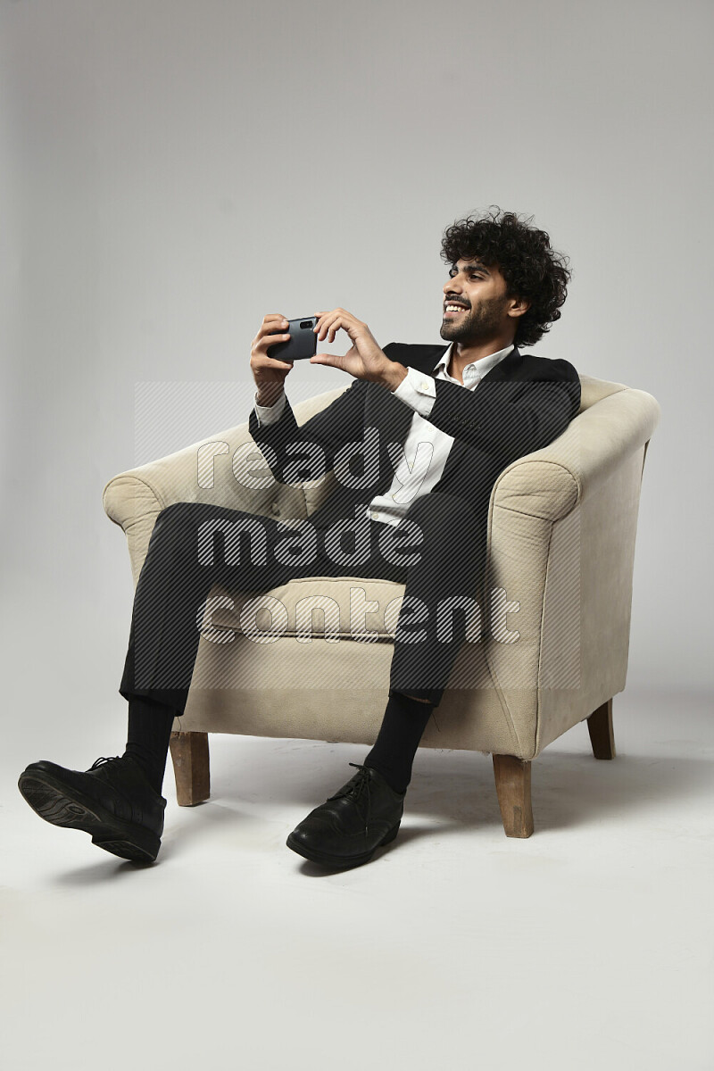 A man wearing formal sitting on a chair shooting with his phone on white background