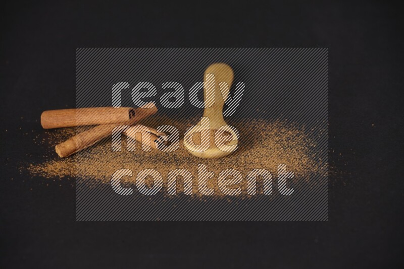 Cinnamon powder in a wooden spoon and cinnamon sticks beside it on black background