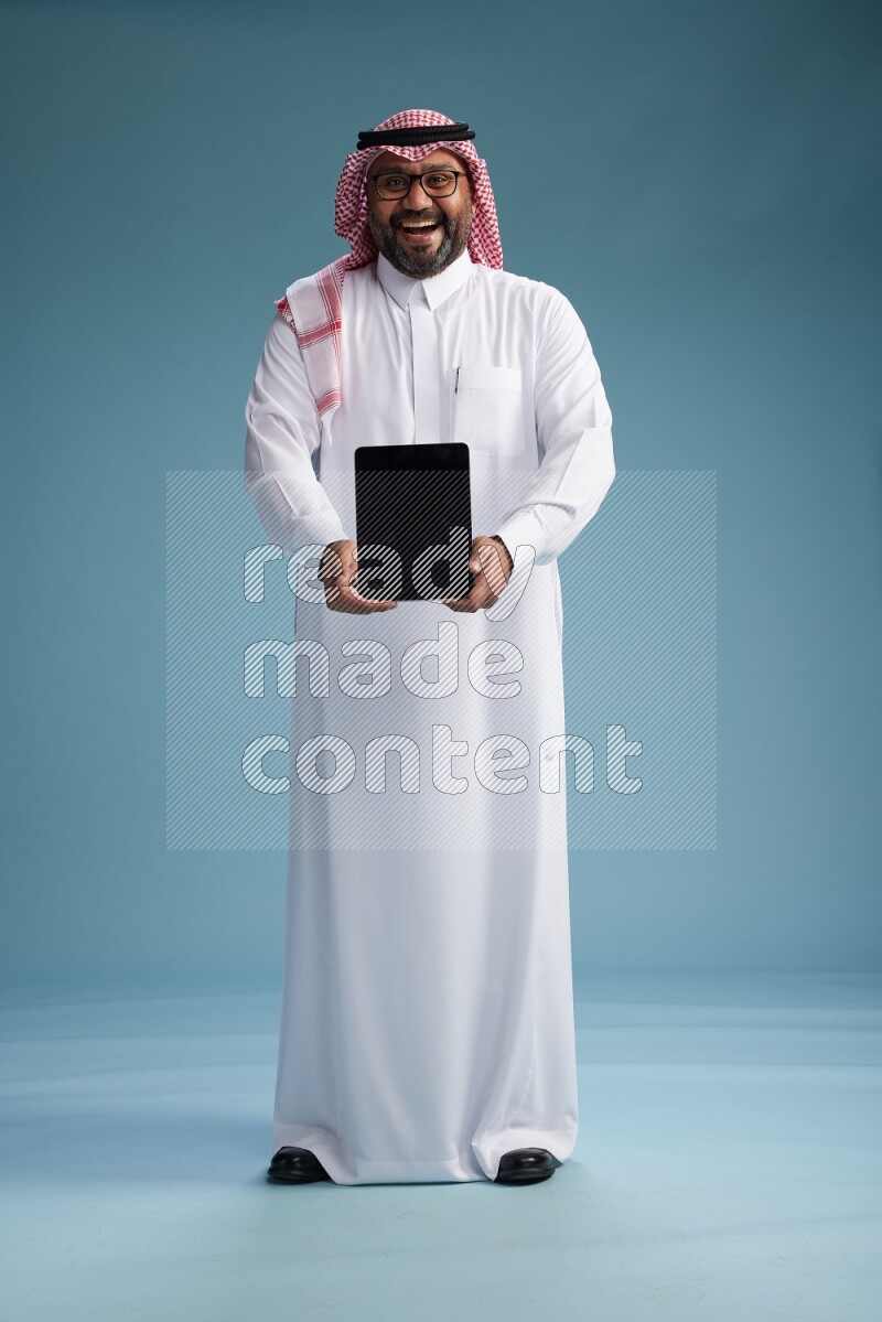 Saudi Man with shimag Standing holding a tablet on blue background
