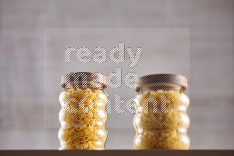 Raw pasta in glass jars on beige background