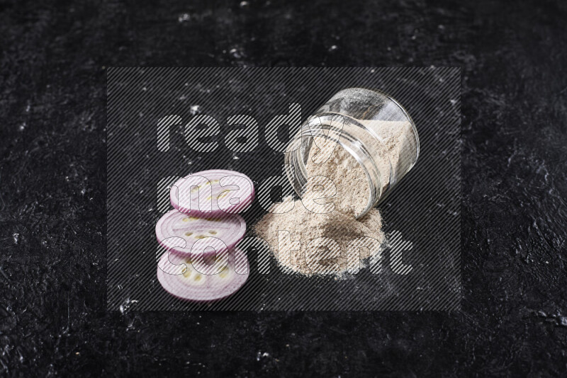 A glass jar full of onion powder flipped with some spilling powder on black background