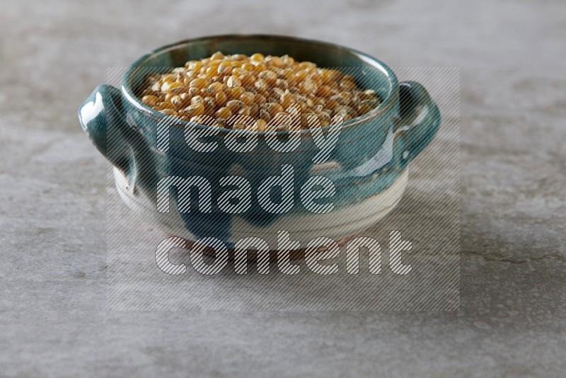 corn kernel in a multi-colored handheld ceramic bowl on a grey textured countertop