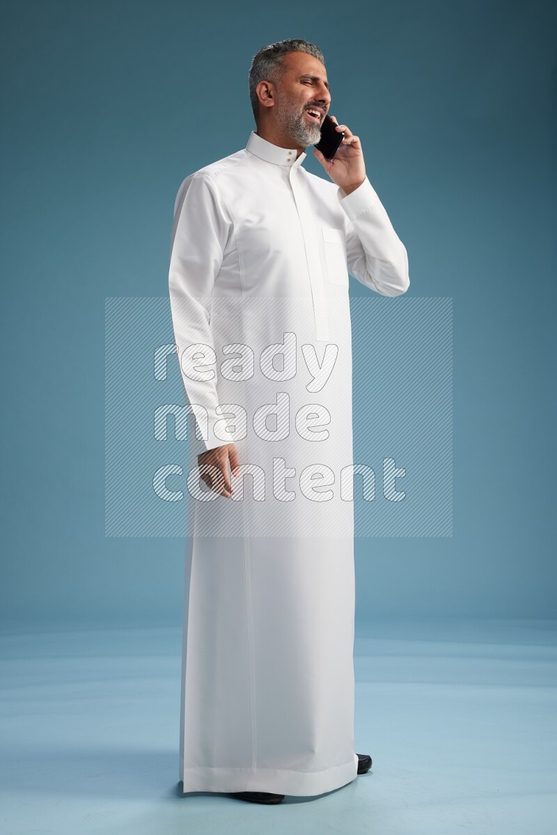 Saudi man wearing thob talking on the phone on blue background
