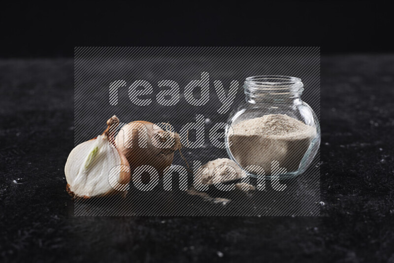 A glass jar full of onion powder on black background