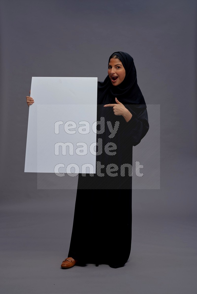 Saudi woman wearing Abaya standing holding white board on gray background