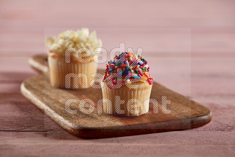 Vanilla mini cupcake topped with sprinkles on a wooden board