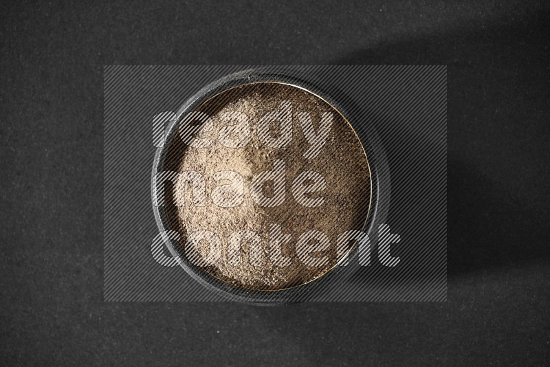 A black pottery bowl full of black pepper powder on black flooring