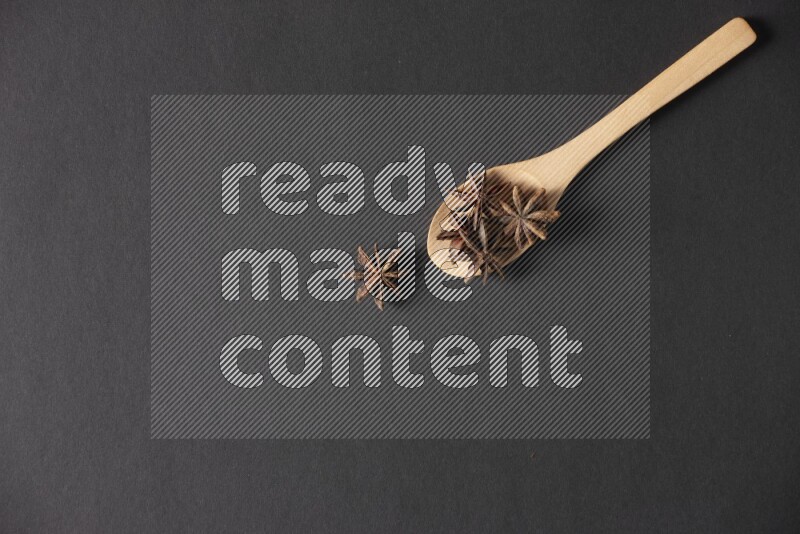 اليانسون النجمي في ملعقة خشبية فوق اليانسون النجمي الذي يغطي الإطار على أرضية سوداء