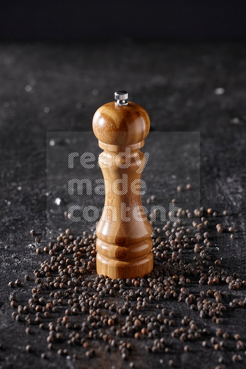A wooden grinder with black pepper beads on a textured black flooring