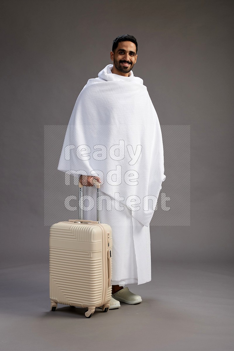 A man wearing Ehram Standing holding traveling bag on gray background