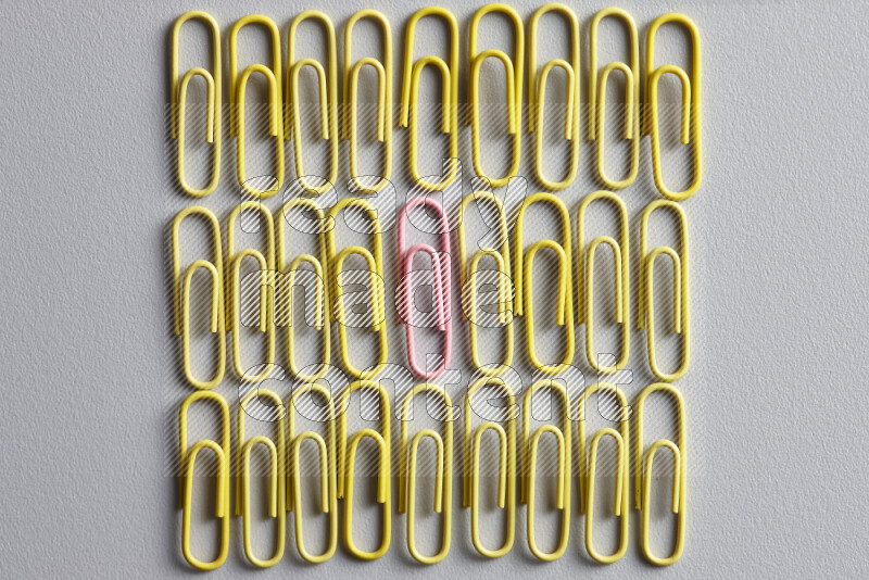 A pink paperclip surrounded by bunch of yellow paperclips on grey background