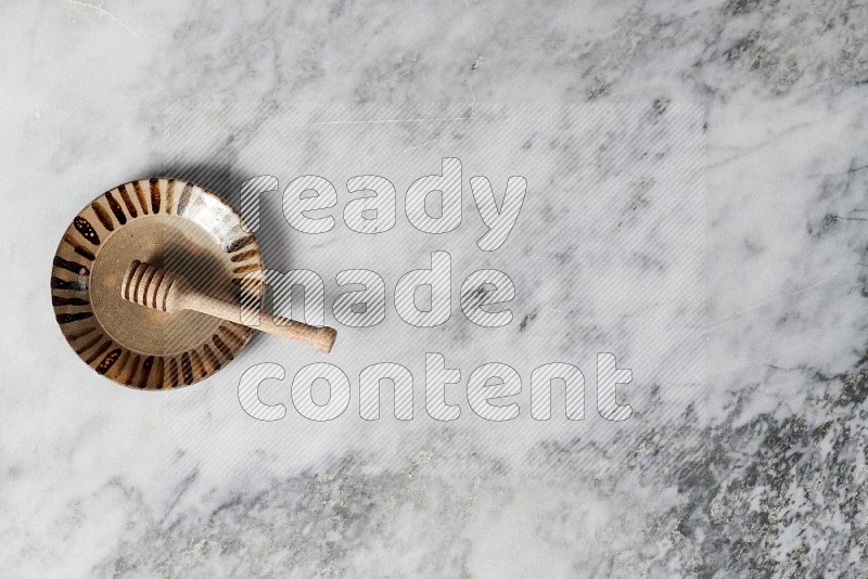 Multicolored Pottery Plate with wooden honey handle in it, on grey marble flooring, Top View