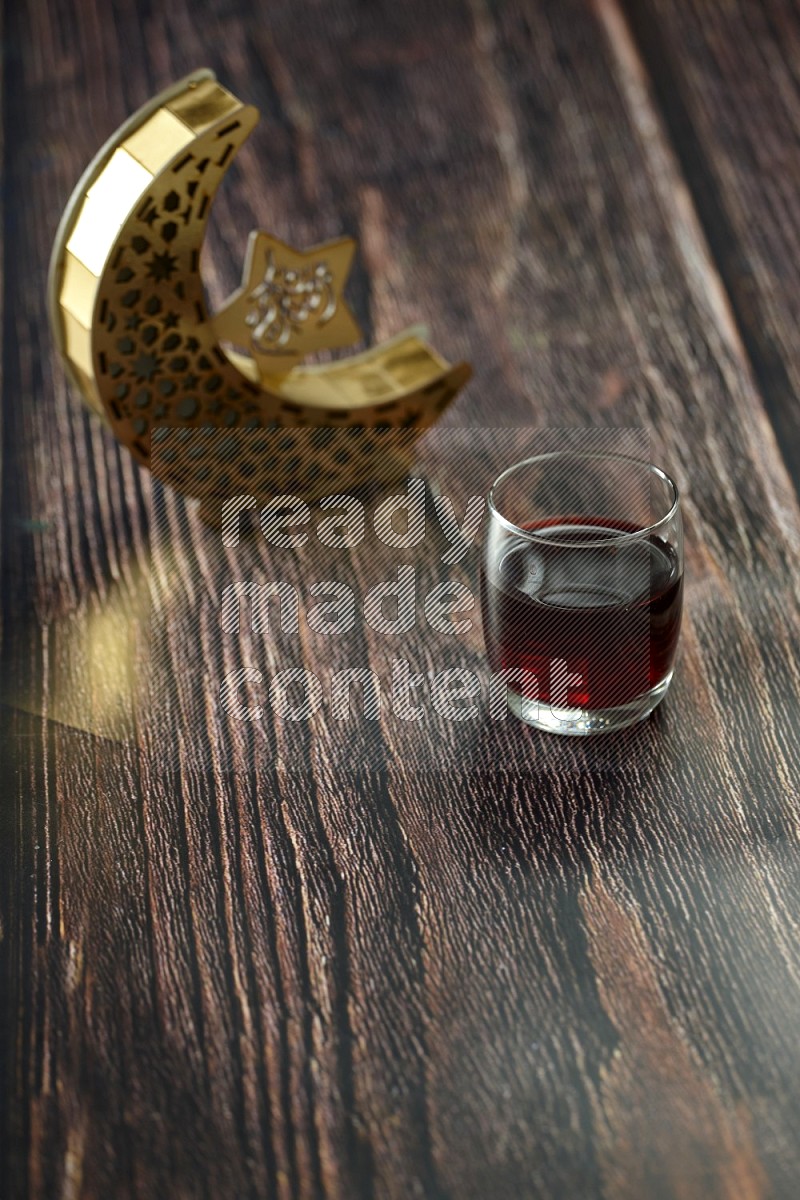 A crescent lantern with drinks, dates, nuts, prayer beads and quran on brown wooden background