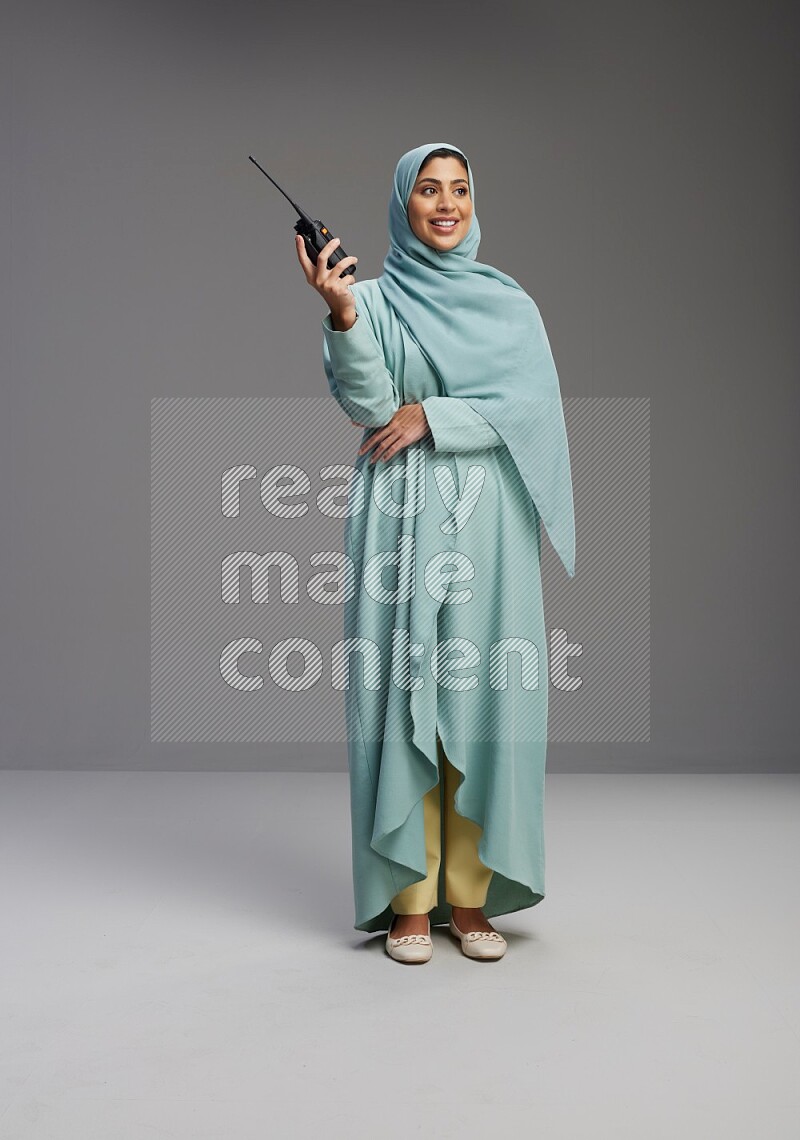 Saudi Woman wearing Abaya standing holding walkie-talkie on Gray background