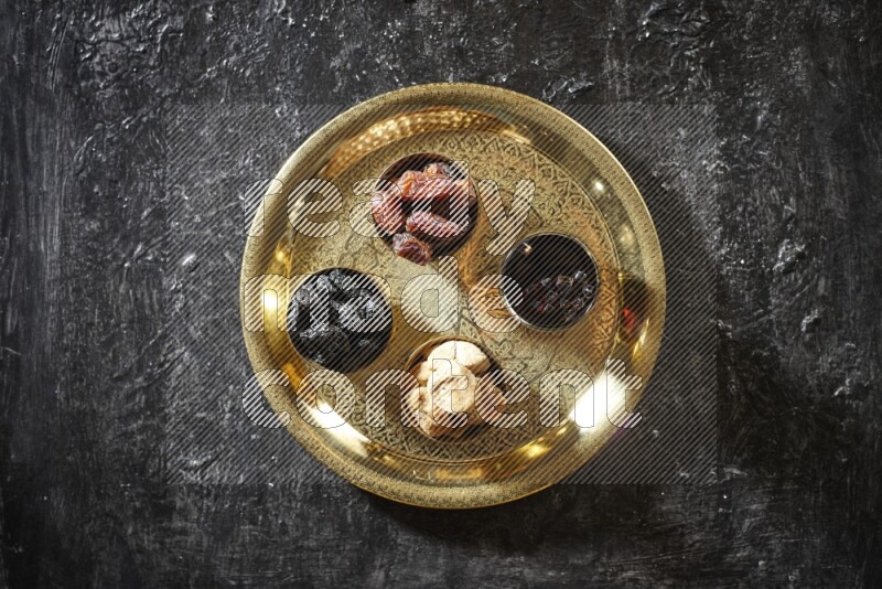 Dried fruits in metal bowls with tamarind on a tray in dark setup