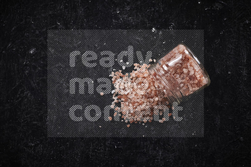 A glass jar full of coarse himalayan salt crystals on black background