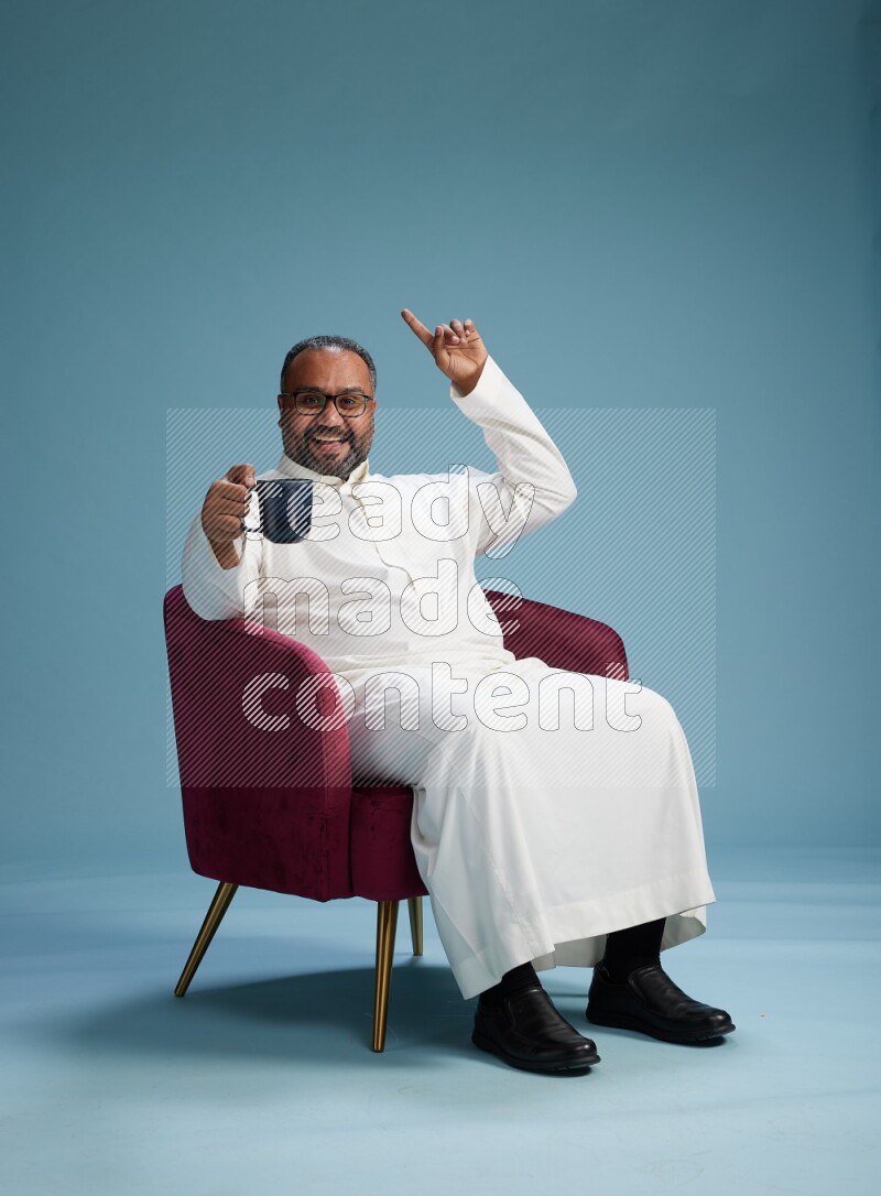 Saudi Man without shimag sitting on chair drinking coffee on blue background