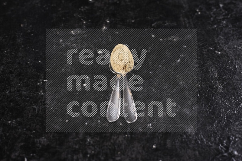 Two metal spoons full of ground ginger powder on black background