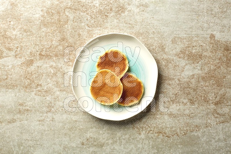 Three stacked plain mini pancakes in a bicolor plate on beige background