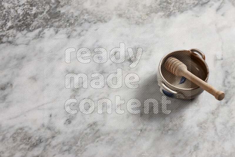 وعاء فخاري متعدد الألوان مع ملعقة عسل خشبية بداخله على خلفية من الرخام الرمادي