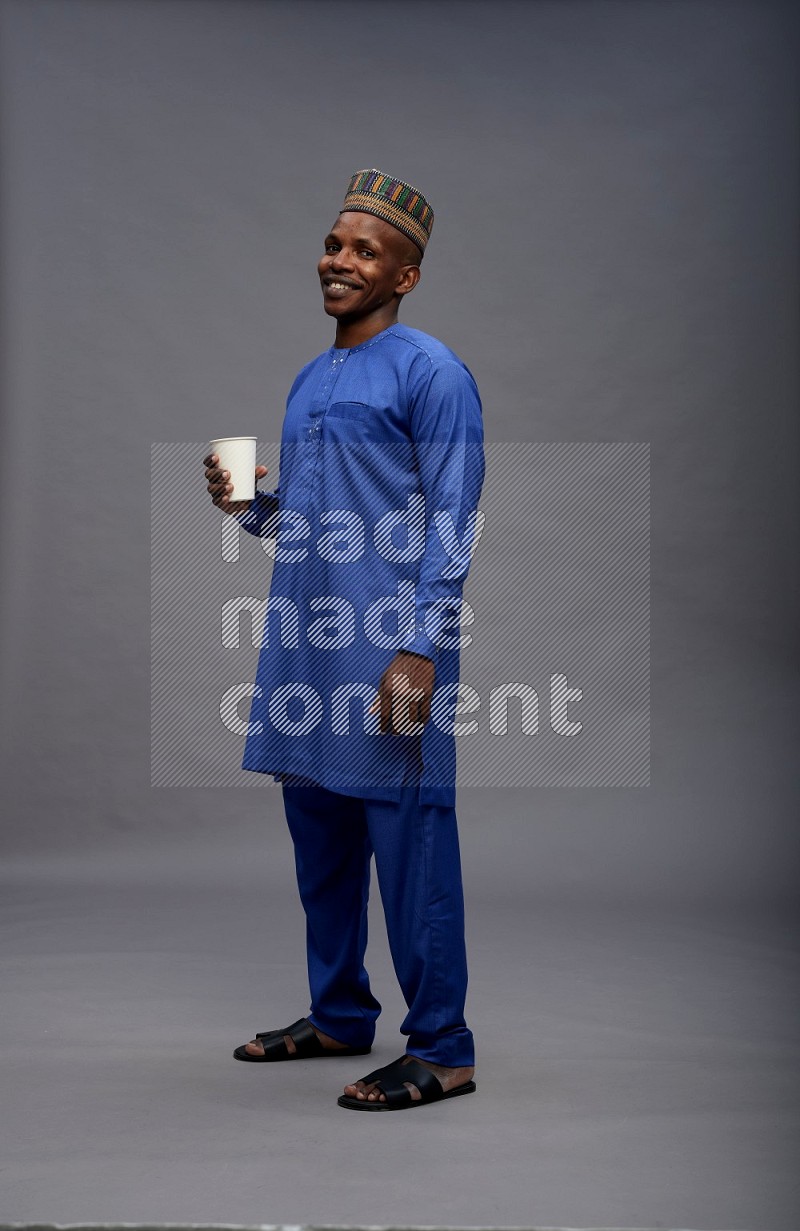 Man wearing Nigerian outfit standing holding paper cup on gray background