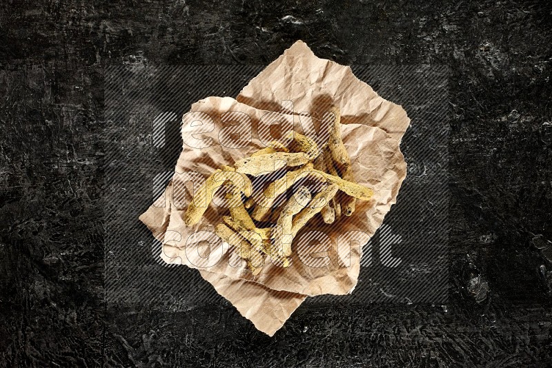 Dried turmeric whole fingers in a crumpled piece of paper on textured black flooring