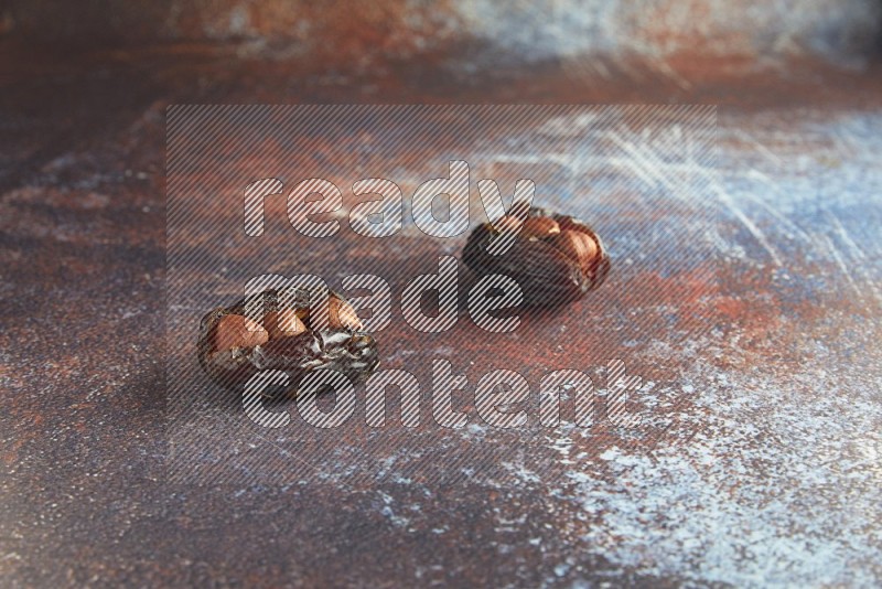 two hazelnut stuffed madjoul dates on a rustic reddish background