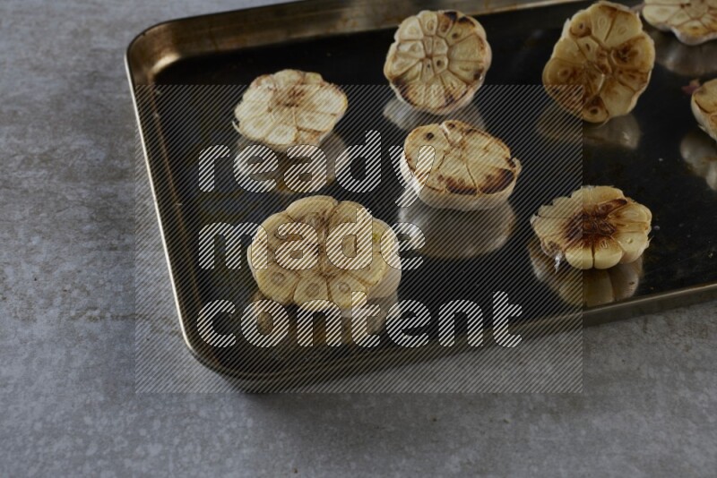half's roasted garlic in a stainless tray on a grey textured countertop
