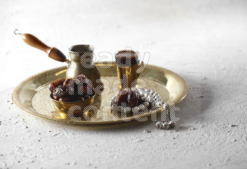 Dates in a metal bowl with coffee and prayer beads on a tray in a light setup