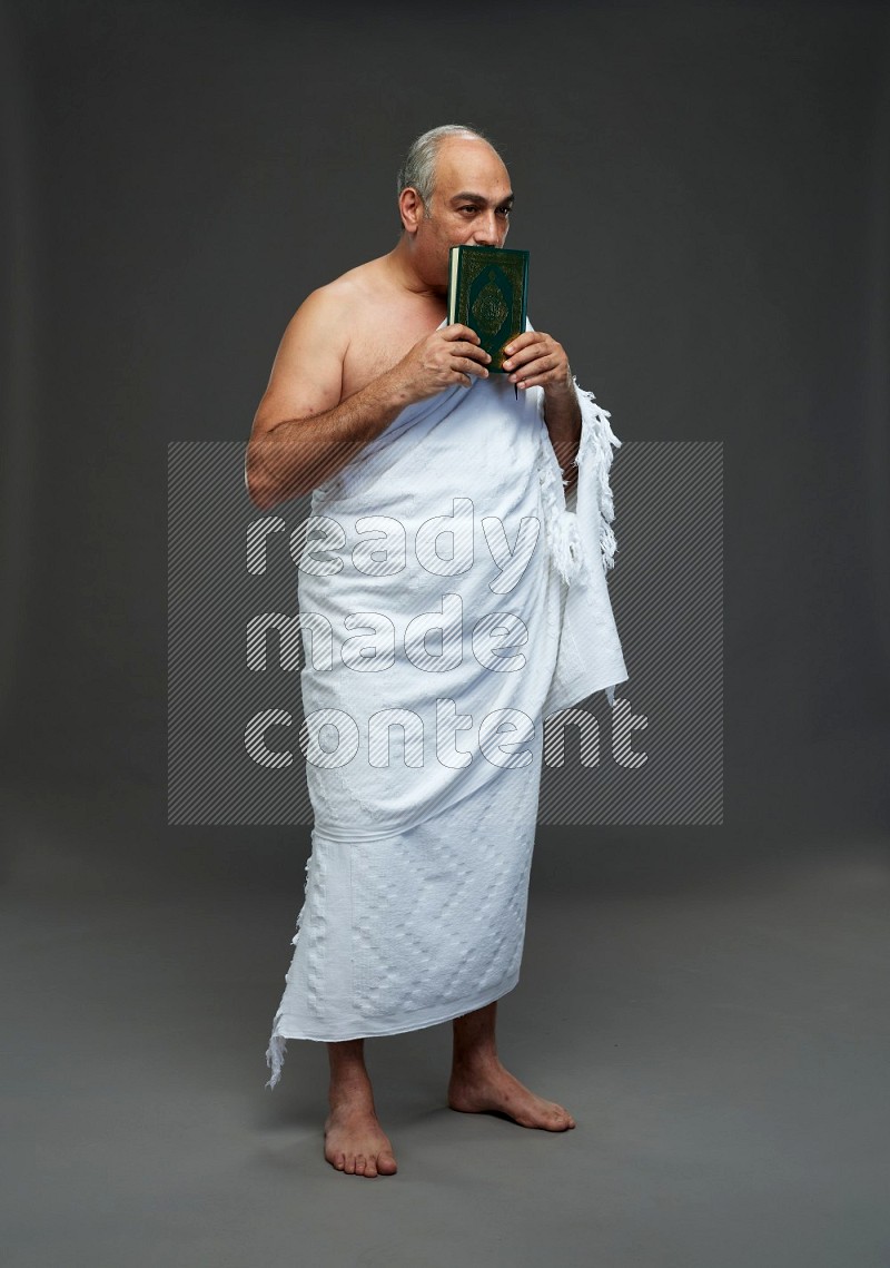 A man wearing Ehram Standing reading quran on gray background
