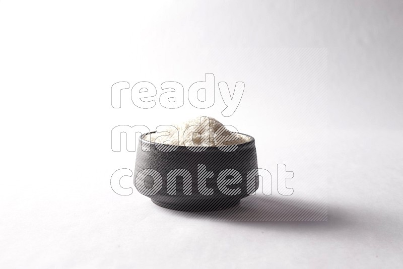 Desiccated coconuts in a black pottery bowl on white background