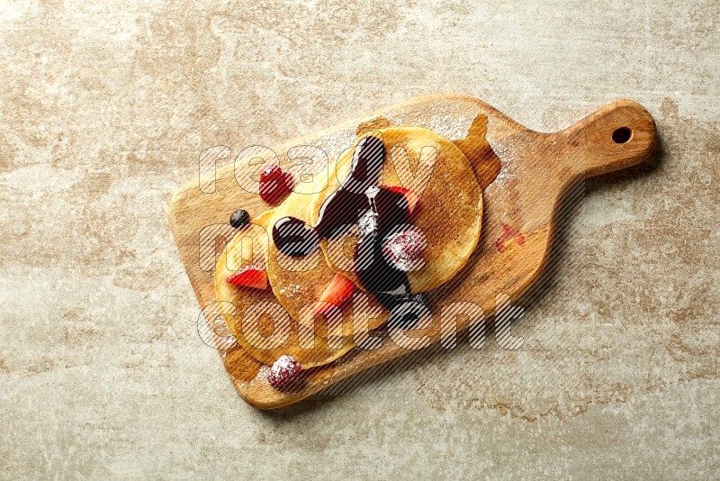Three stacked mixed berries pancakes on a wooden board on beige background