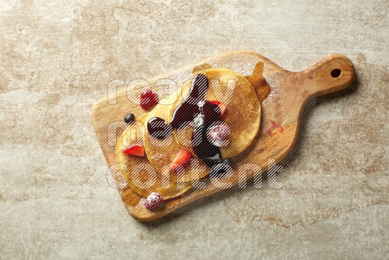 Three stacked mixed berries pancakes on a wooden board on beige background