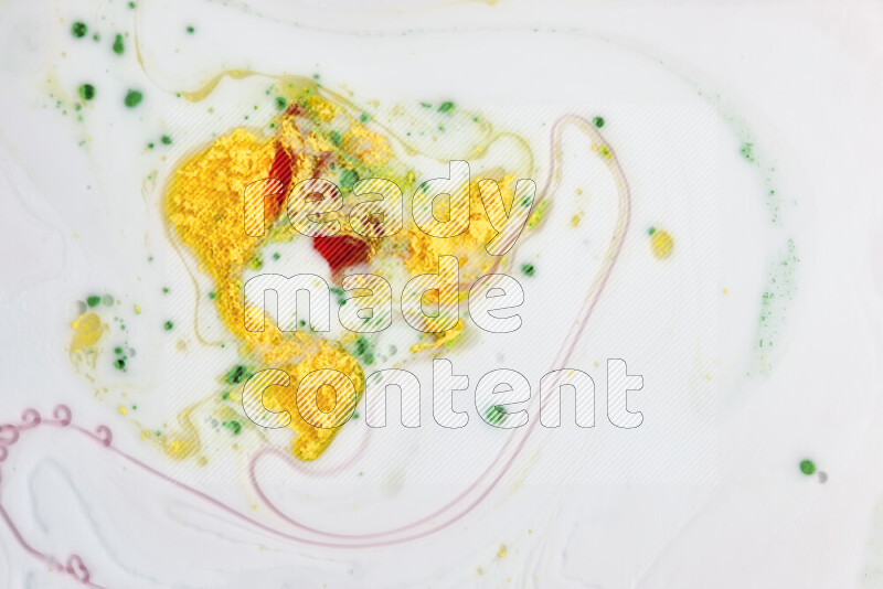 The image captures a splatter of yellow, red and green paint over a white backdrop