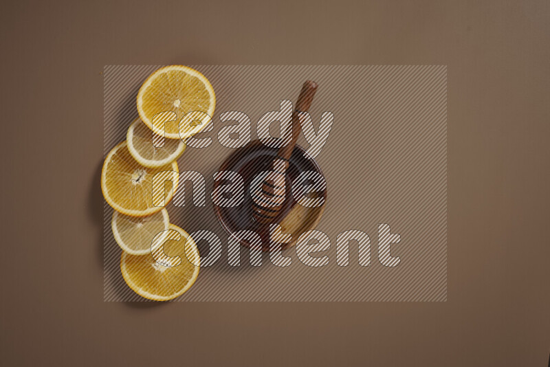 A bowl full of honey with some of citrus fruits such as lemon and orange on a beige background