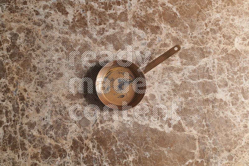 Top View Shot Of A Small Copper pan On beige Marble Flooring