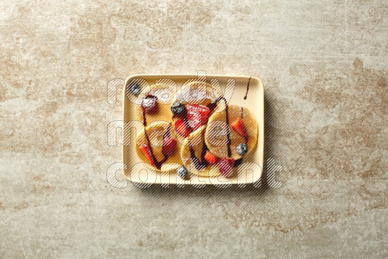 Five stacked mixed berries mini pancakes in a rectangular plate on beige background