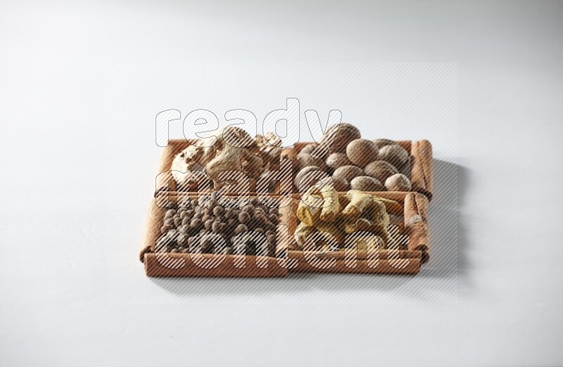 4 squares of cinnamon sticks full of nutmegs, dried ginger, turmeric fingers and allspice on white flooring