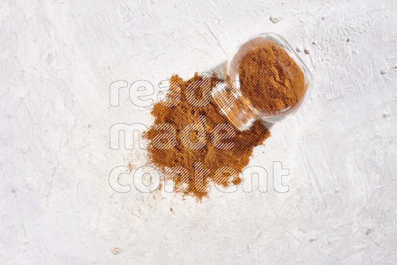 A glass jar full of ground paprika powder flipped with some spilling powder on white background