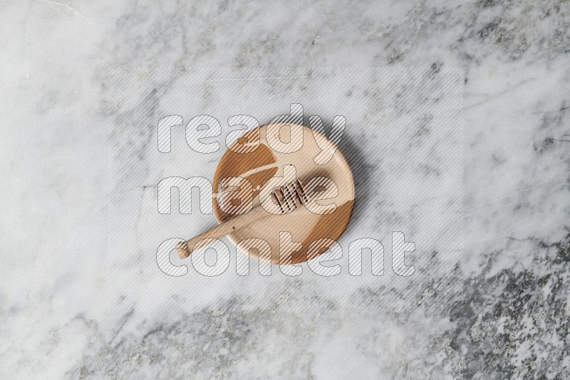 Multicolored Pottery Plate with wooden honey handle in it, on grey marble flooring, Top View