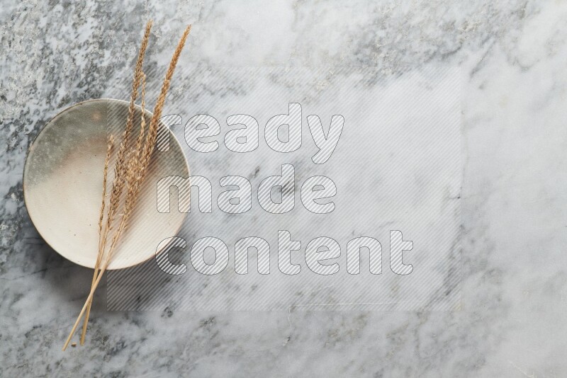 Wheat stalks on multicolored pottery plate on grey marble background